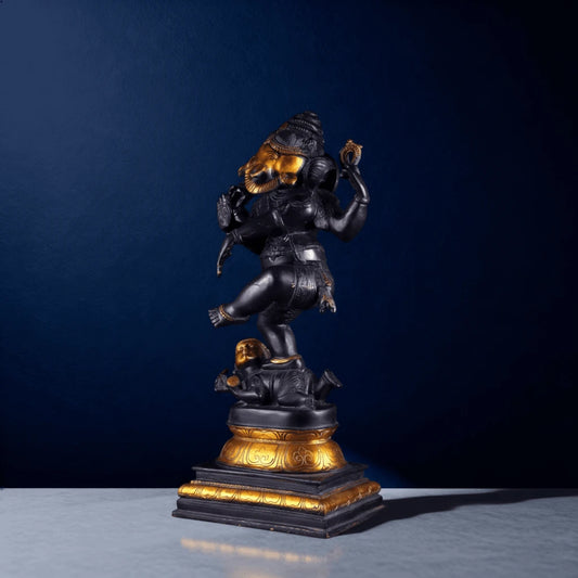 Side view of black and gold dancing Ganesha statue with raised leg on demon figure pedestal