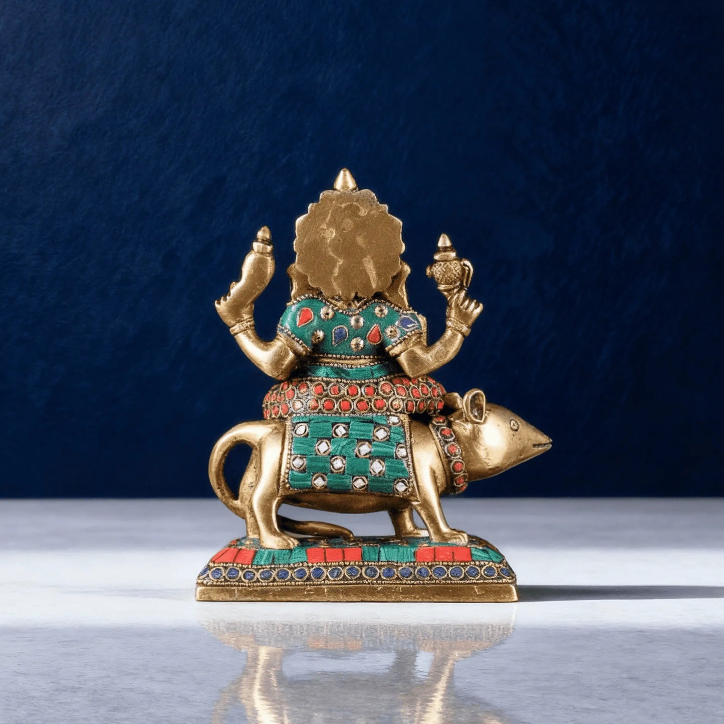Brass Ganesha idol riding mouse vahana with multicolor stone inlay work front view on blue background