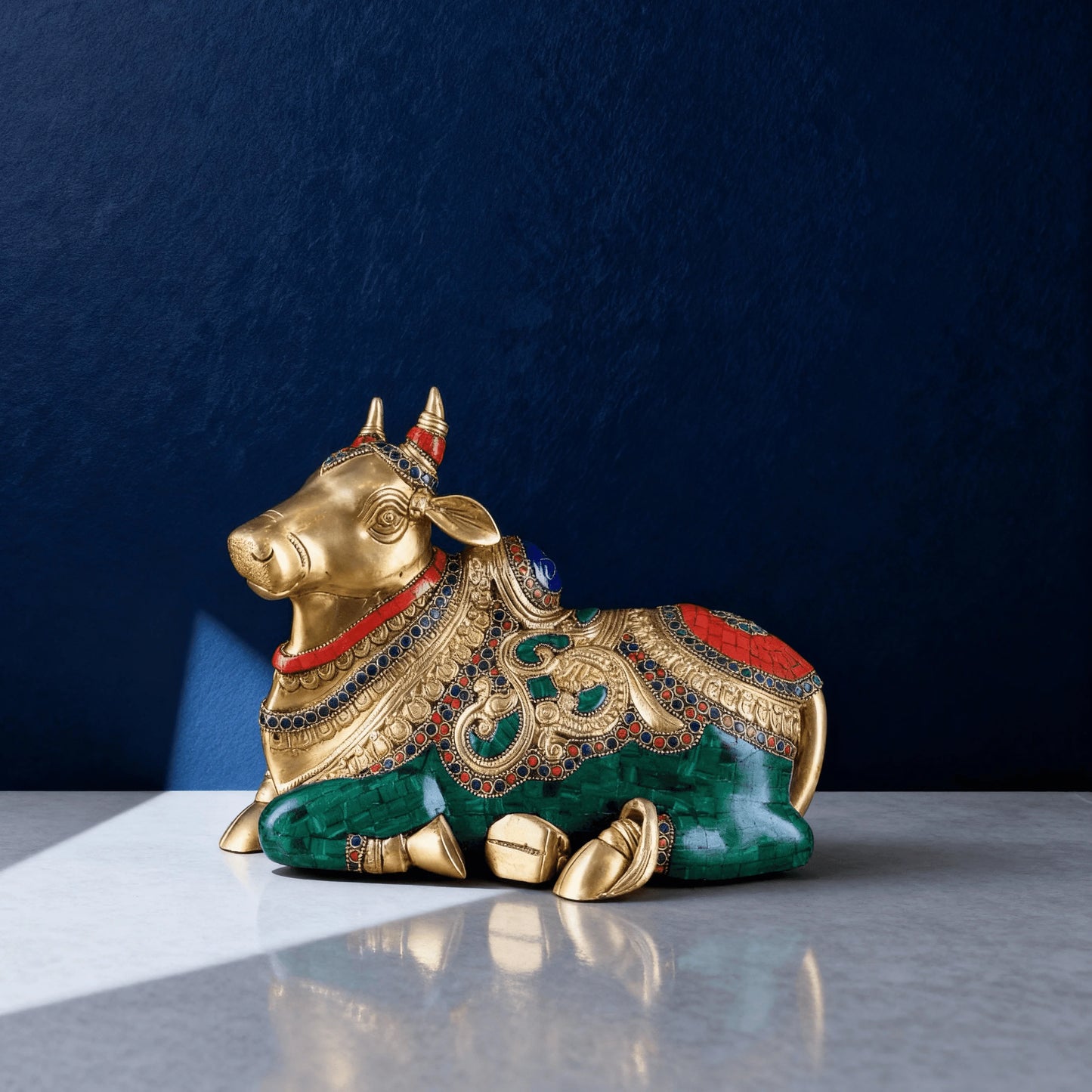 Handcrafted pure brass Nandi statue with detailed red and green stone inlay, polished finish, and raised right leg on marble base.