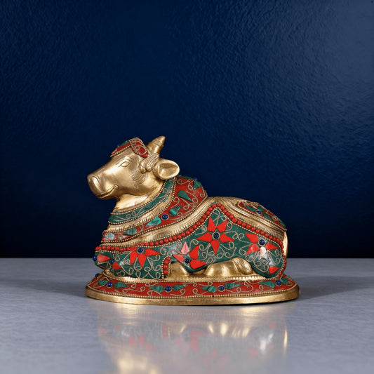 brass meenakari nandi cow idol with red and green stonework on a blue background