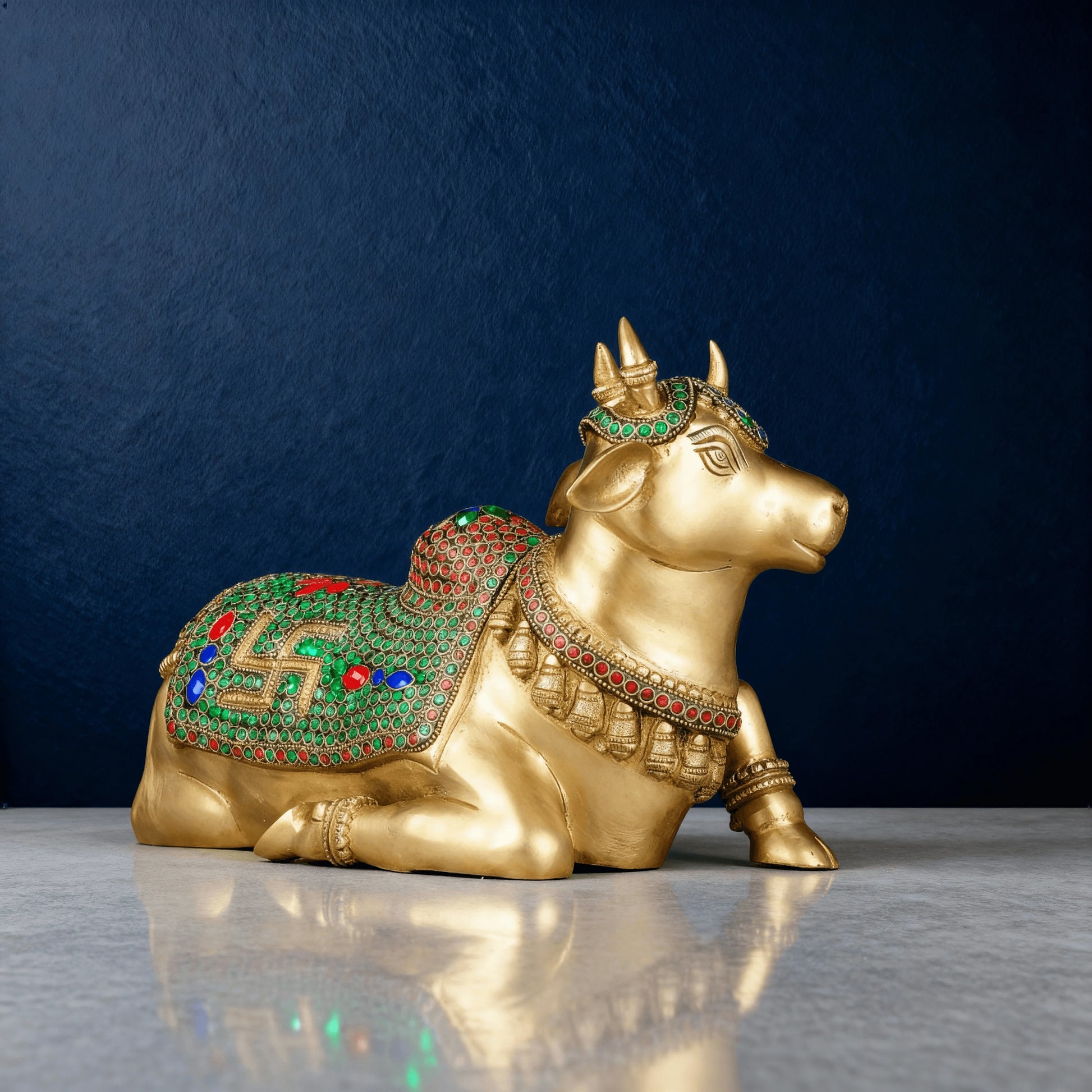 brass Nandi statue with green and red stonework detailing, photographed in studio lighting against a dark blue background