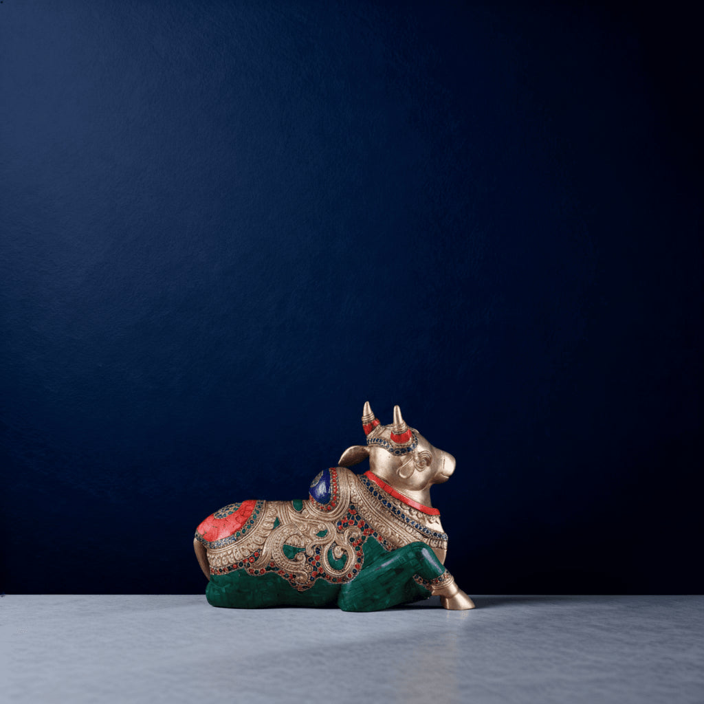 Profile view of Aarvya brass Nandi sculpture with elaborate gemstone accents and handcrafted carvings against a deep blue backdrop.