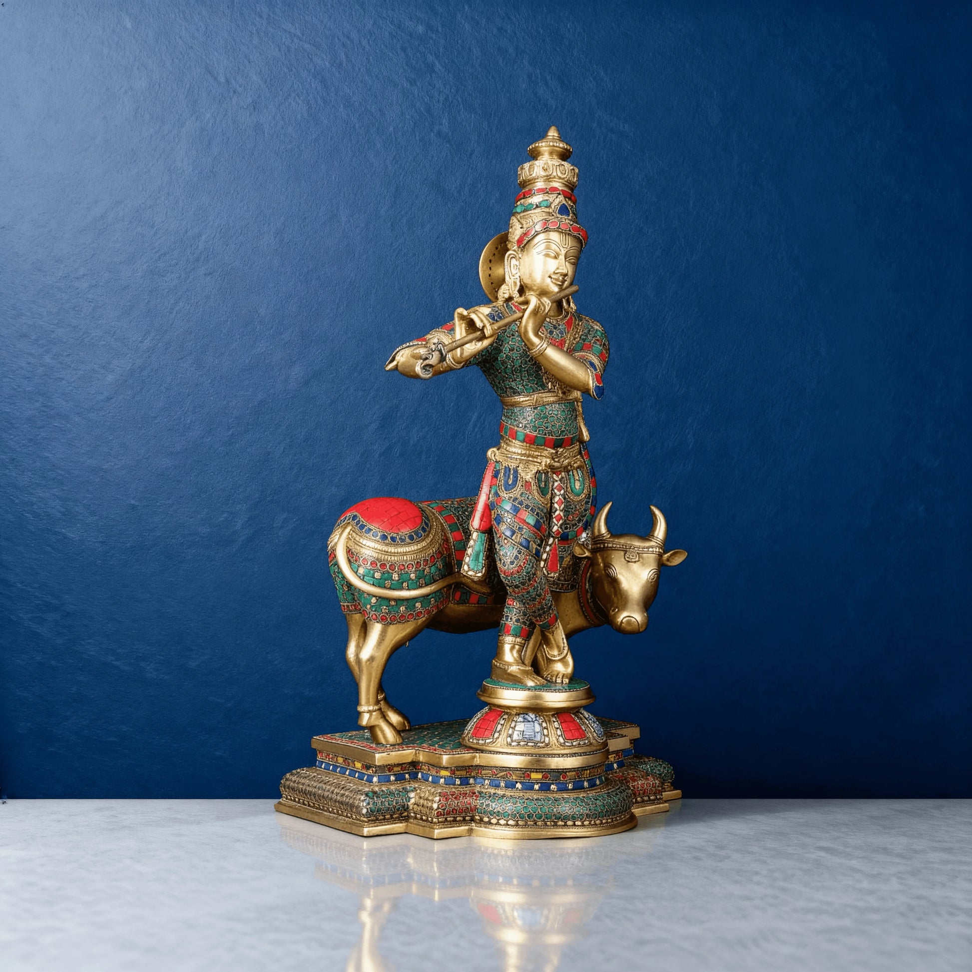 Close-up of Krishna with Cow idol in antique brass, vibrant enamel inlay work, on carved pedestal base
