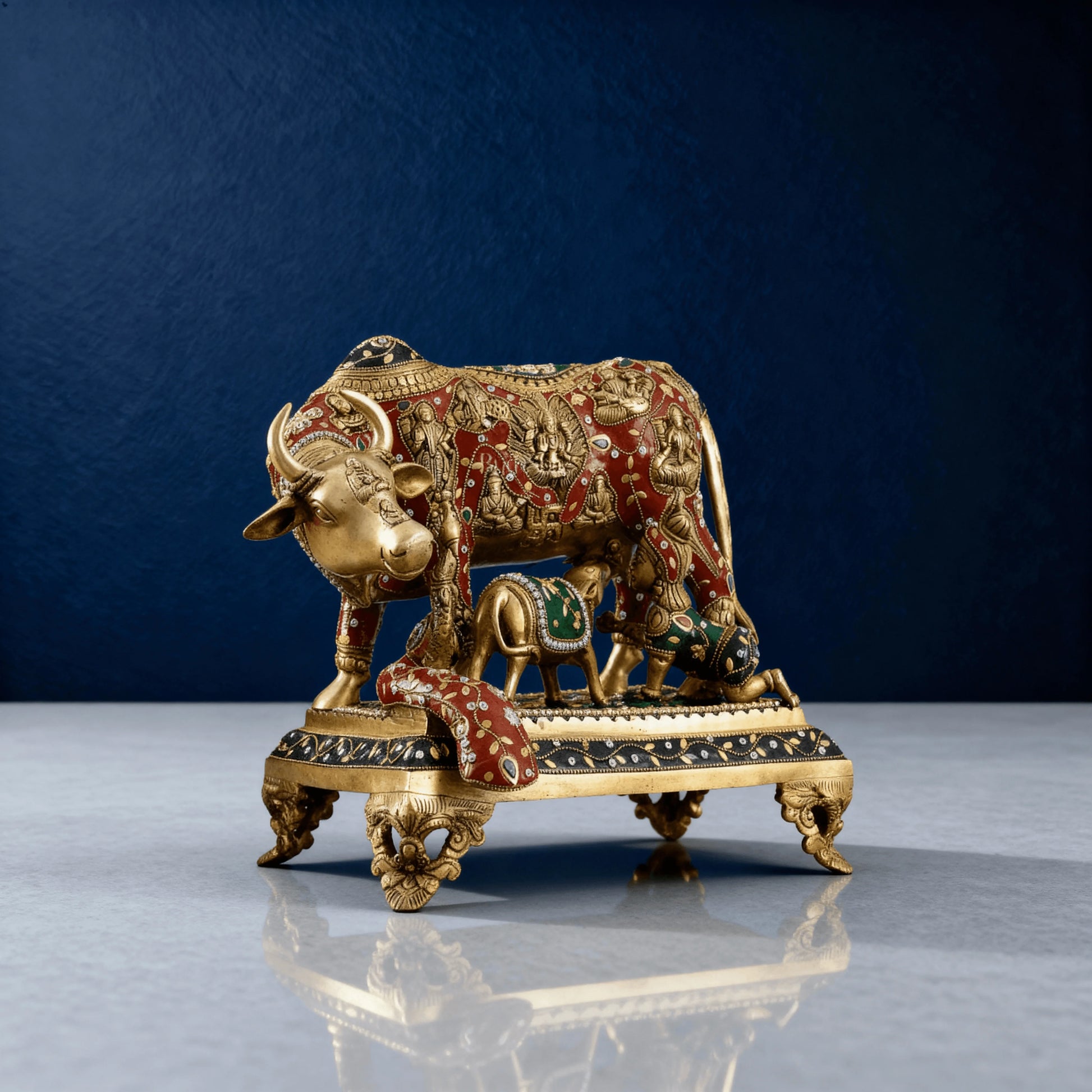 Front angled view of brass Kamadhenu cow and calf statue with ornate carvings and painted accents, gold finish