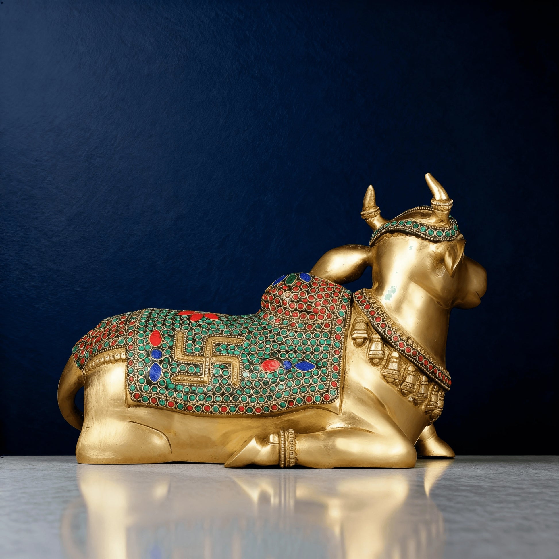 side view of stone-inlaid brass Nandi idol showing detailed saddle design with green, red, and blue mosaic patterns