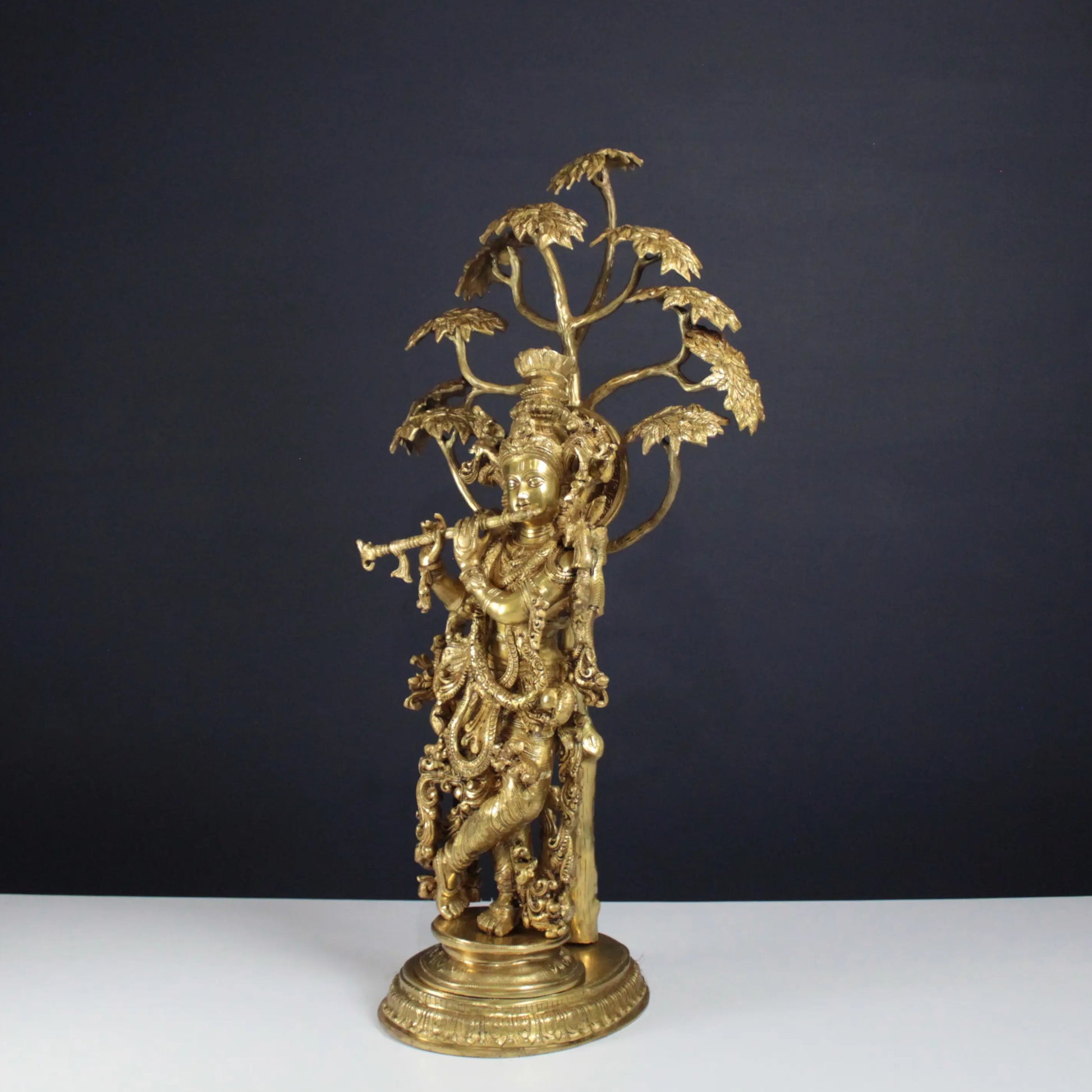 Gold decorative Krishna Idol on a white table with a dark background