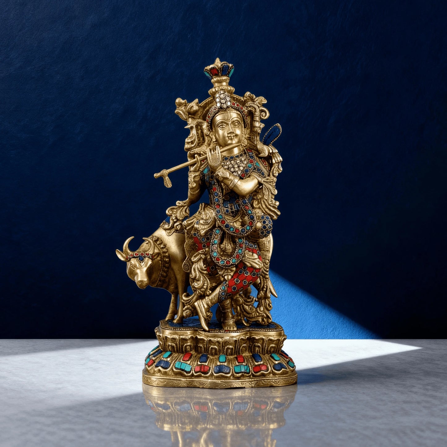Profile shot of pure brass Krishna and cow idol with colorful stone inlays, on carved circular pedestal base