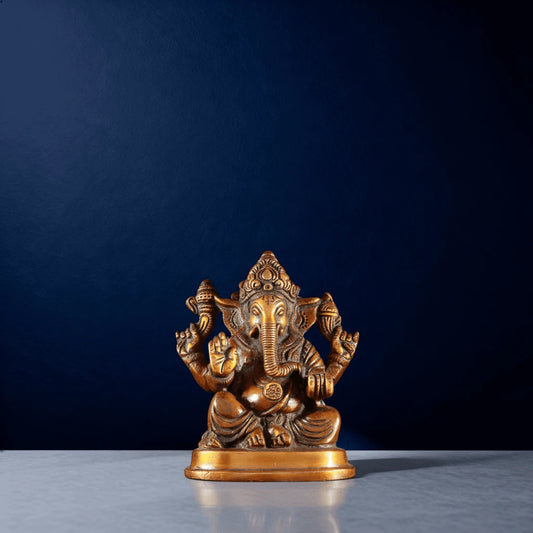 Front-facing brass Ganesh murti seated in blessing pose with ornamental crown and four arms
