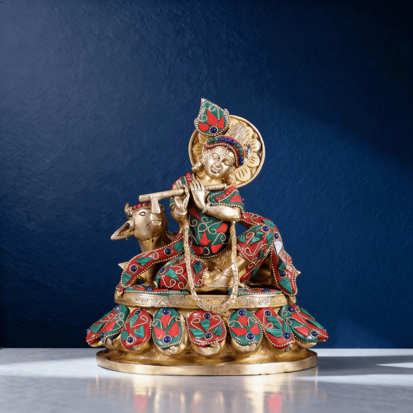 Front view of Krishna with cow brass idol featuring red and green meenakari, handcrafted on lotus-style base.
