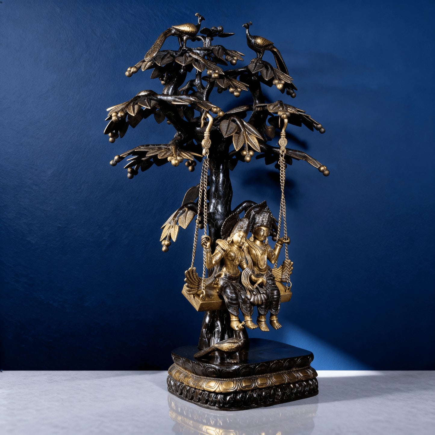 Side view of Radha Krishna brass swing idol beneath ornate tree