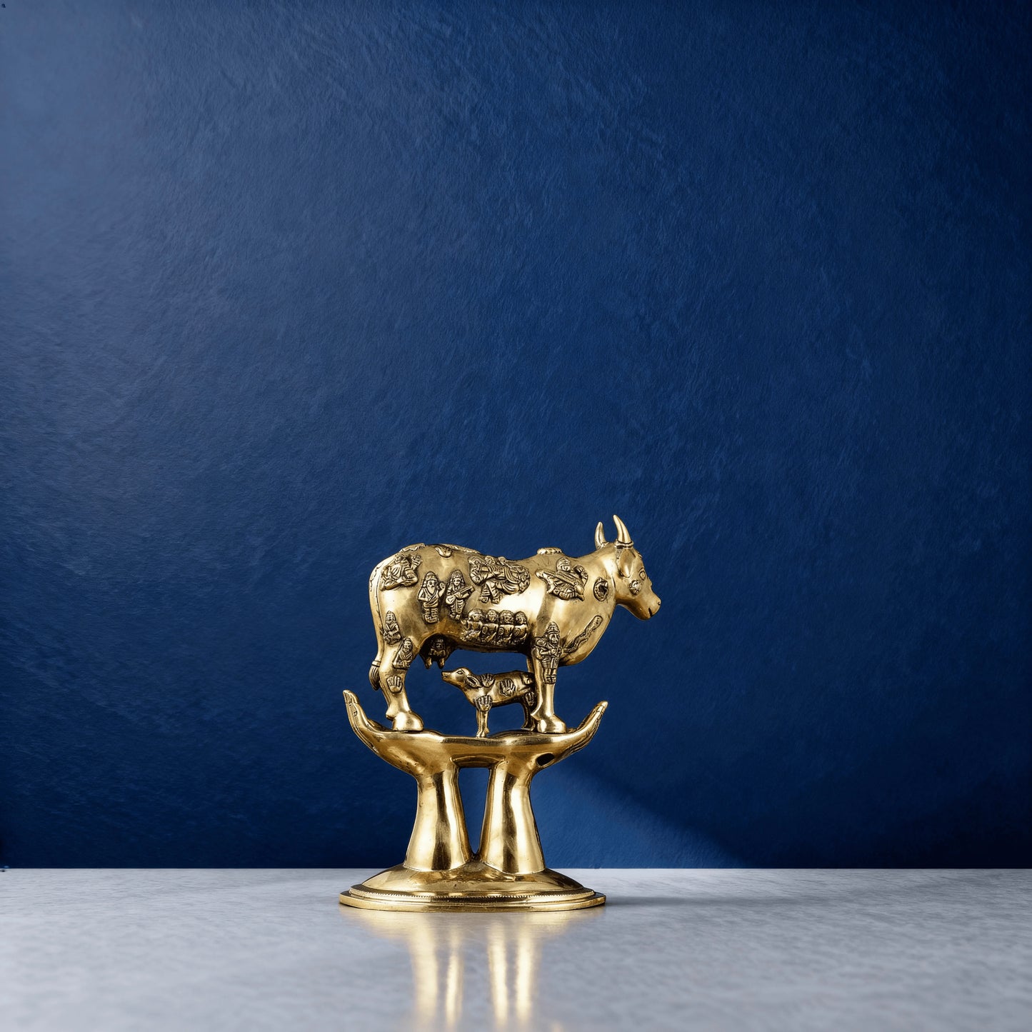 Brass Kamadhenu cow idol with engraved deities and calf on raised hands – traditional Hindu pooja decor