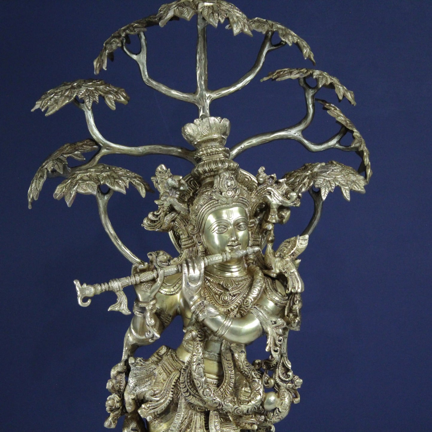 Decorative Brass sculpture of a figure of Krishna  with a tree-like structure on a blue background