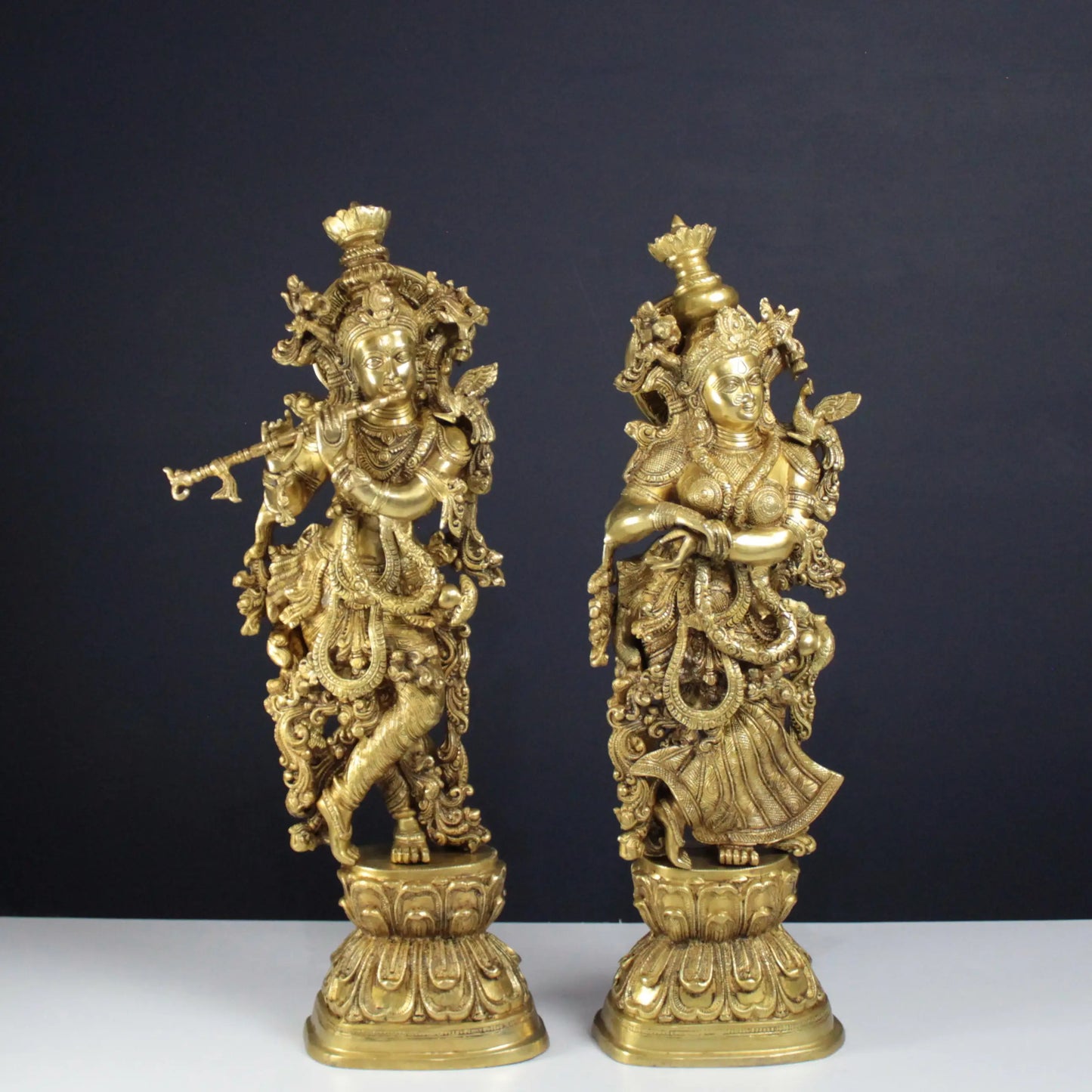 Two Radha Krishna gold statues on a dark background