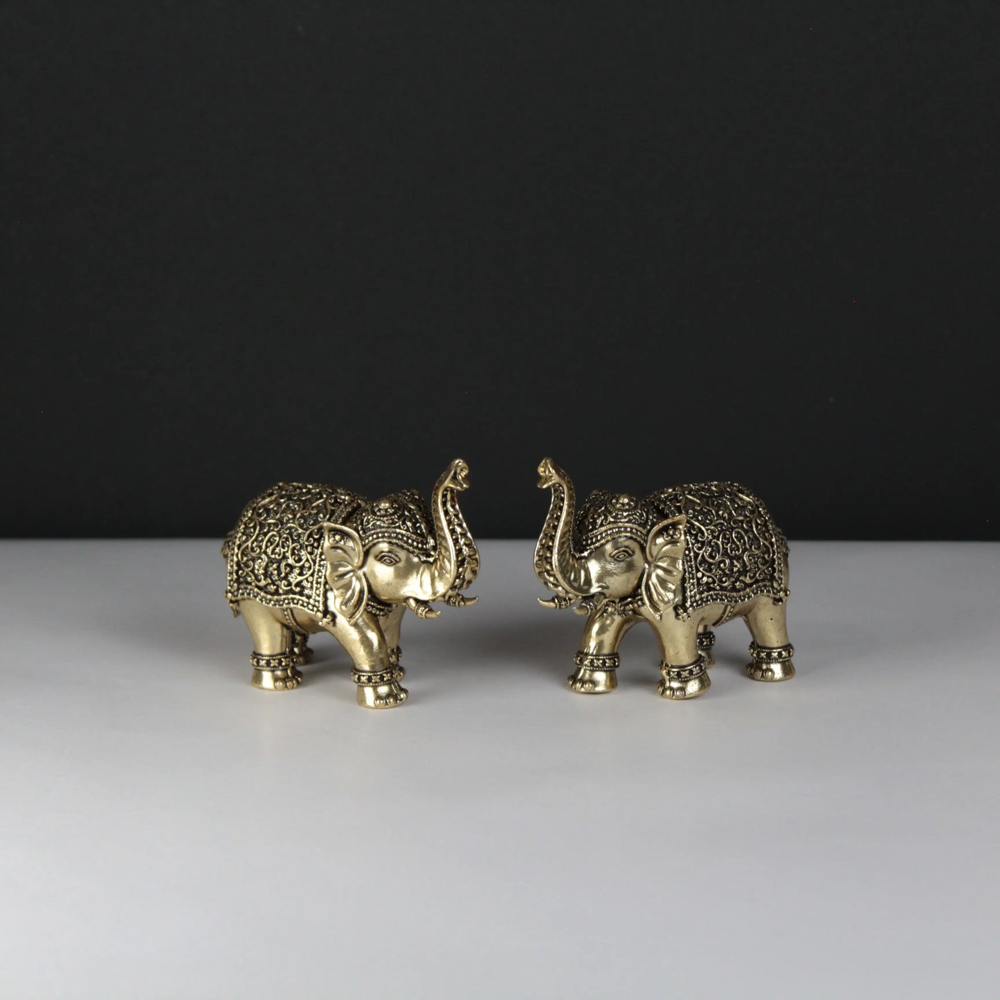 Two ornate gold elephant figurines on a white surface with a black background