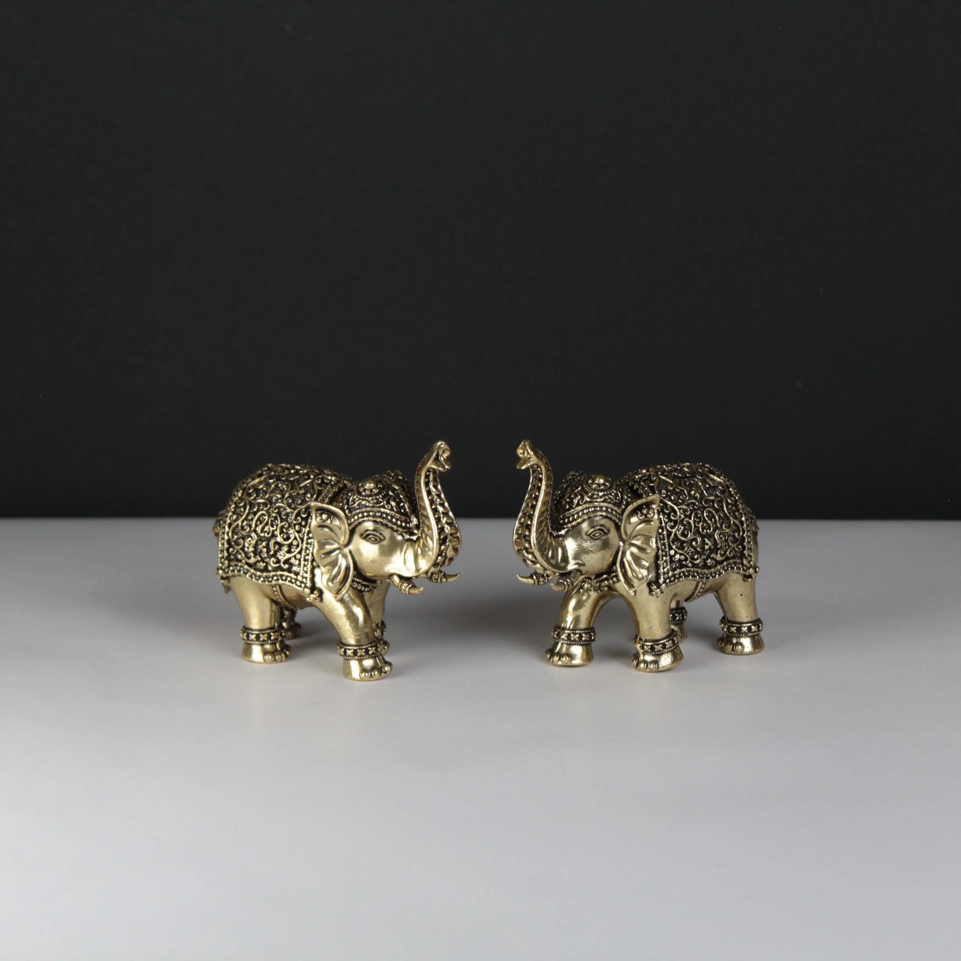 Two ornate gold elephant figurines on a white surface with a black background