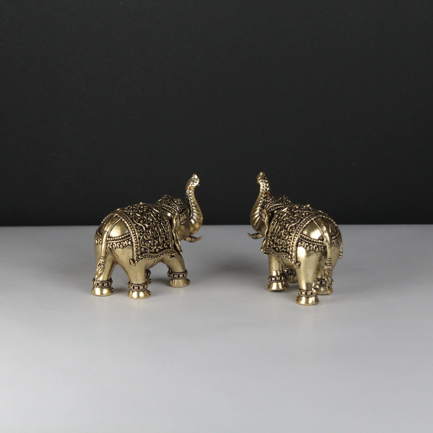 Two ornate gold elephant figurines on a white surface with a black background