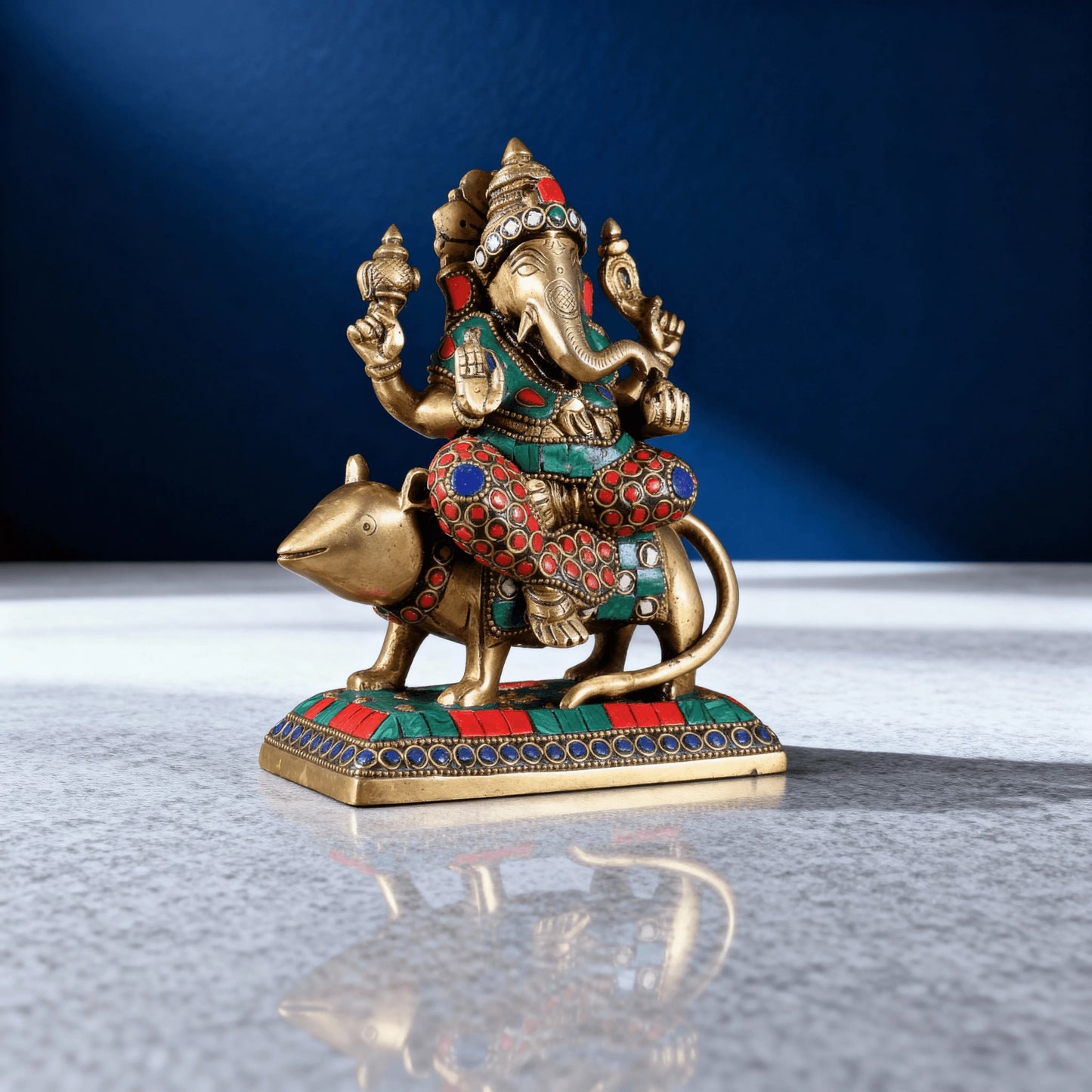 Handcrafted brass Ganesha statue on mouse with red green blue stone detailing side angle studio shot