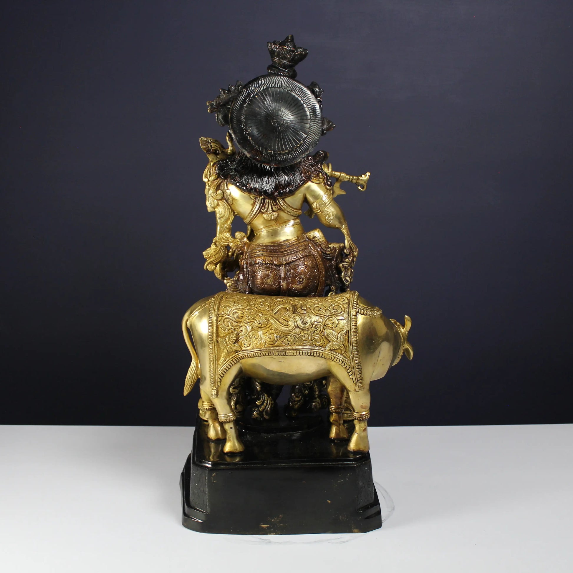 Decorative Krishna statue of a figure on a Cow with intricate details against a dark background