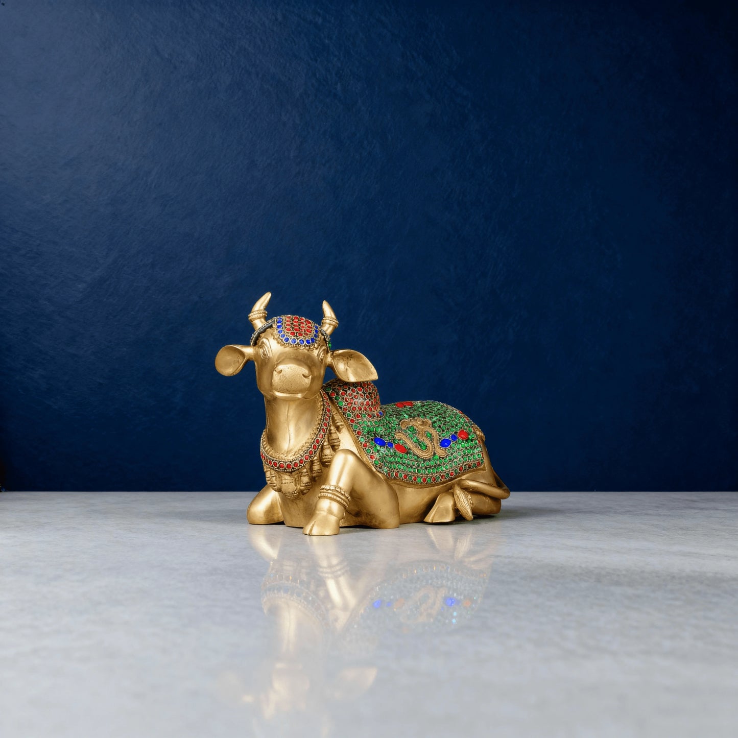 front-angled shot of brass Nandi idol decorated with green and red stones, placed on a clean white surface in studio lighting