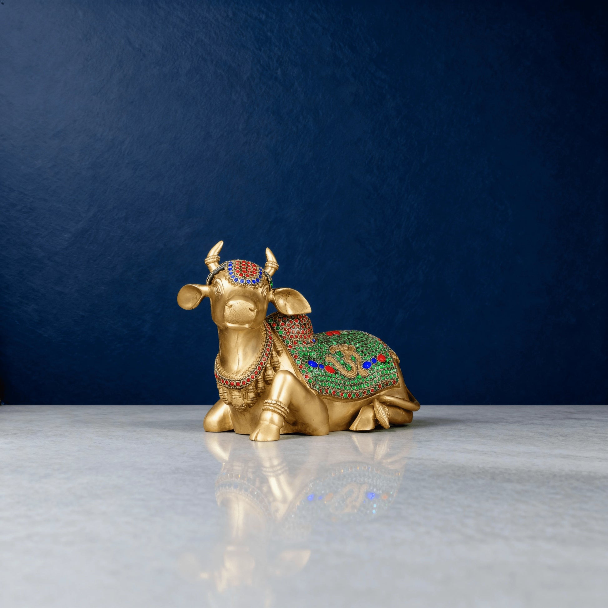 front-angled shot of brass Nandi idol decorated with green and red stones, placed on a clean white surface in studio lighting