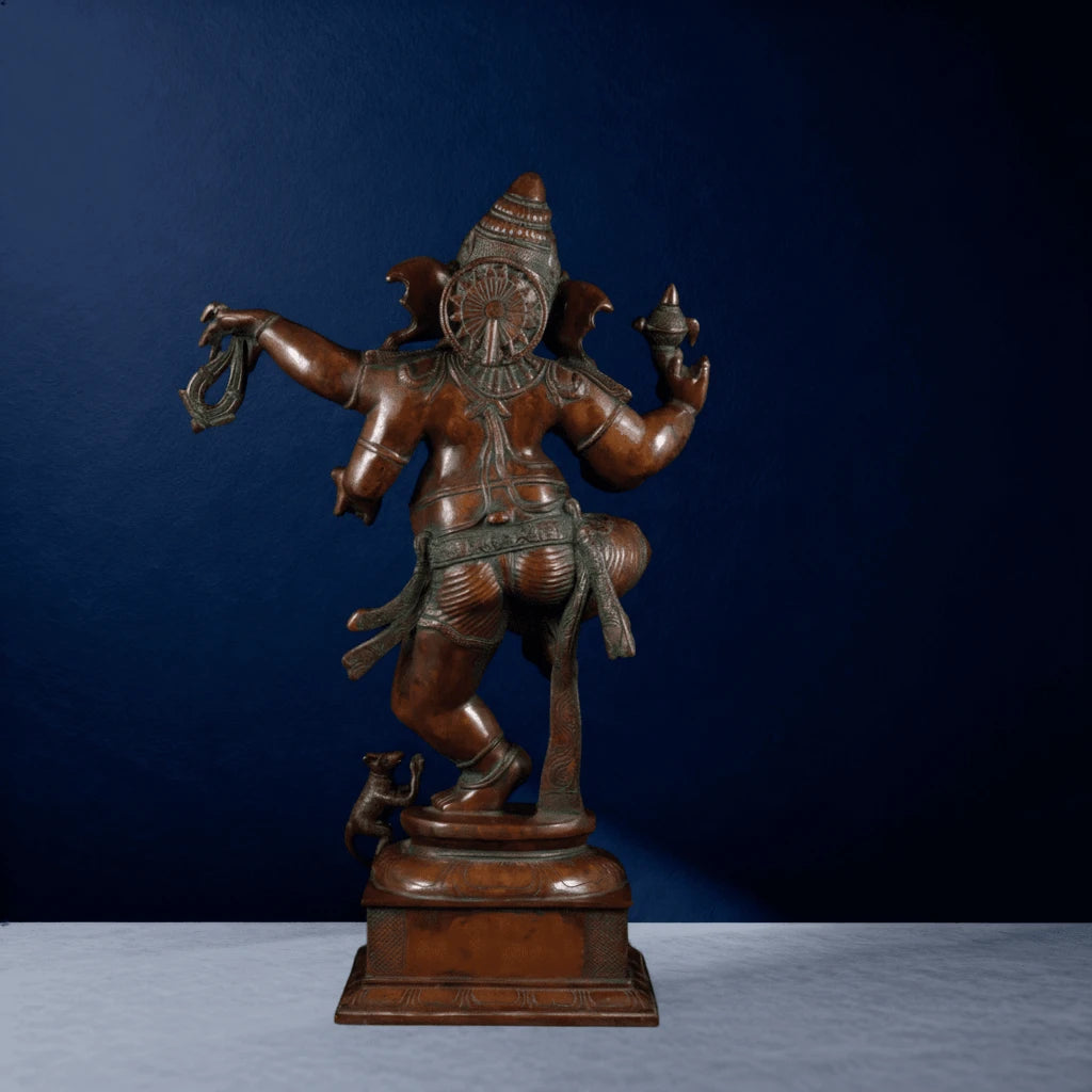 Rear view of brown polished dancing Ganesha statue with intricate carvings and mouse figure on base