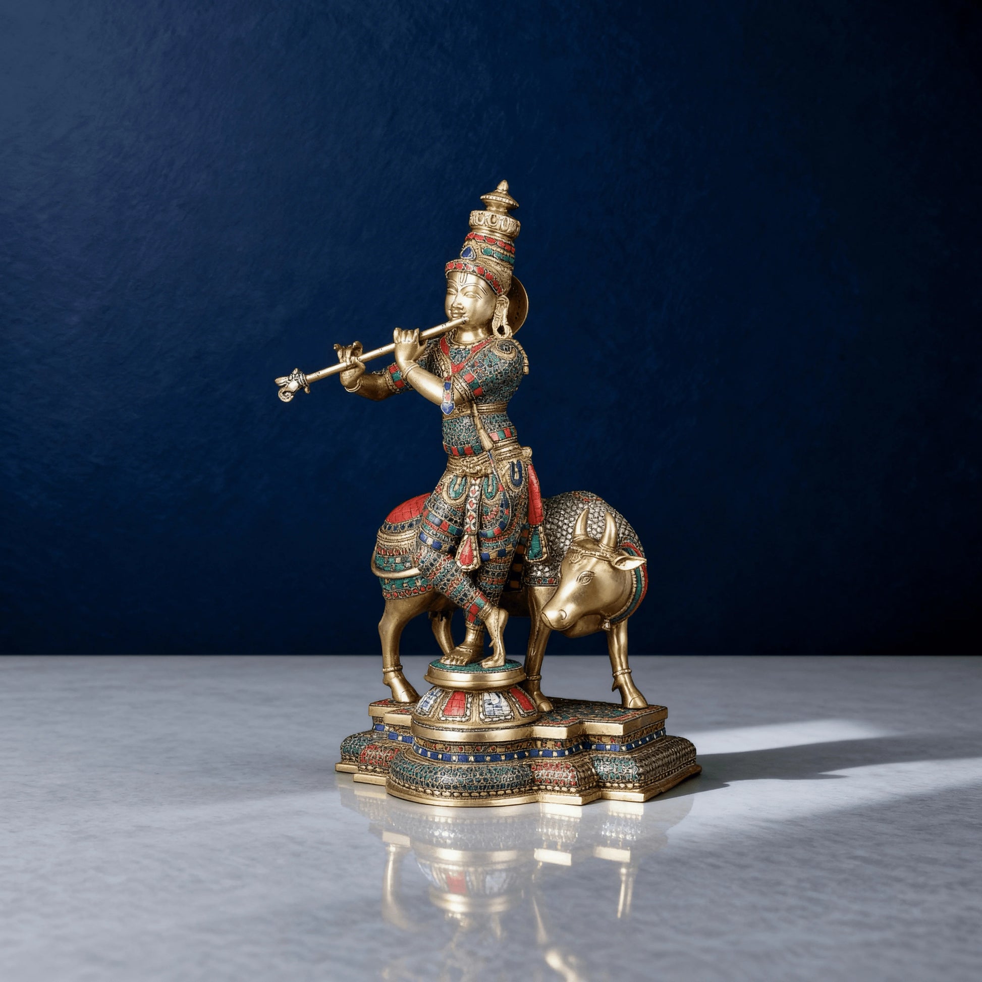Side angle of Krishna playing flute beside cow, pure brass sculpture with red-green meenakari detailing, traditional design