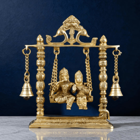 Front view brass Radha Krishna swing statue with carved pillars and bells, elegant handcrafted jhula for home decor.