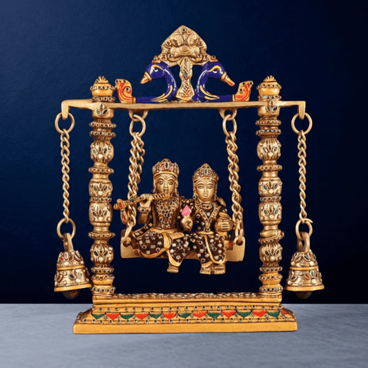 Front view brass Radha Krishna swing idol with meenakari work, peacock arch design, hanging bells and ornate base detailing