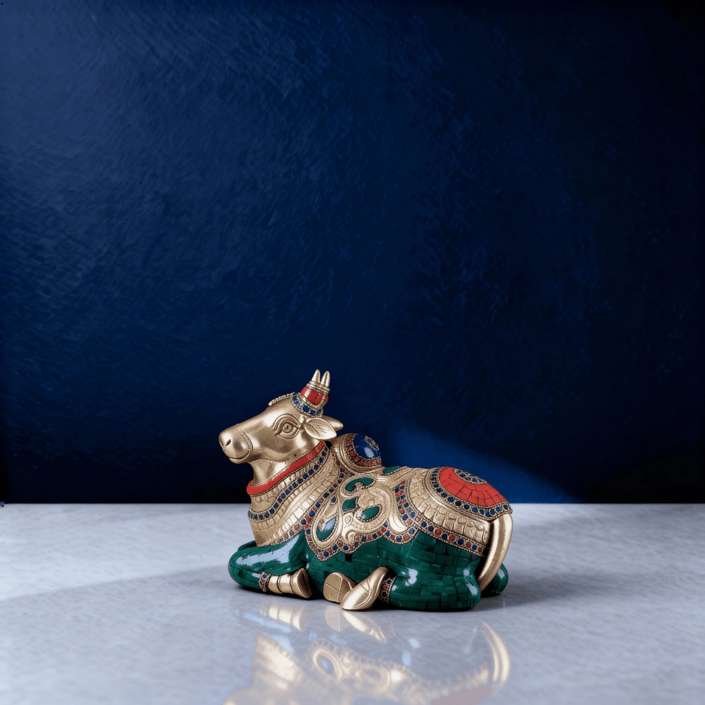 Side angle of pure brass Nandi with vibrant meenakari stone inlay in red, green, and blue tones, placed on smooth marble surface.